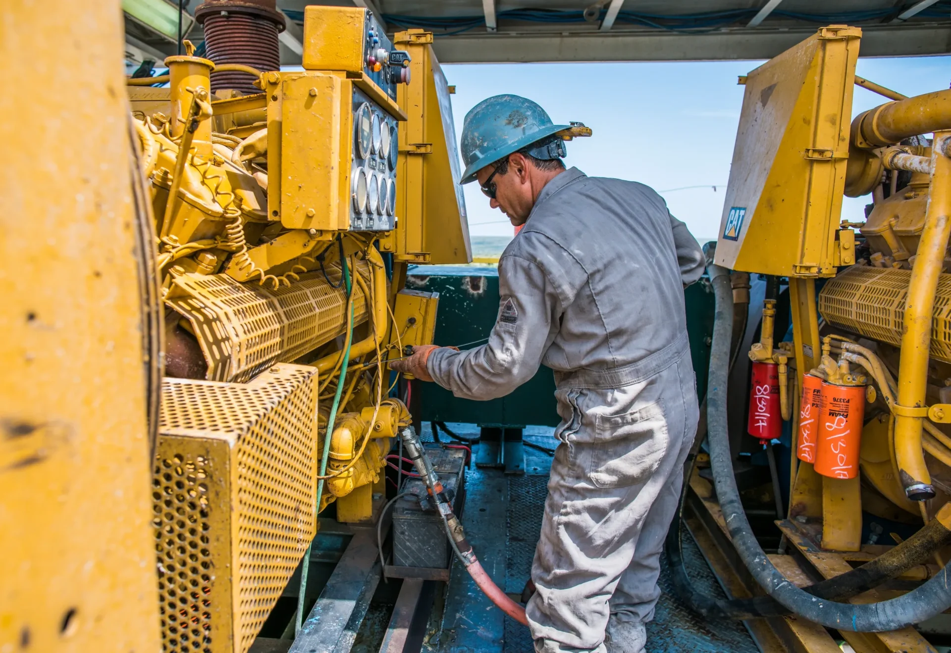 A man in grey work suit and blue hard hat working on machinery.